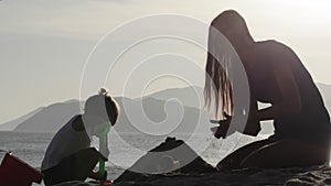 Silhouette of mother and small daughter building sand castles on the beach