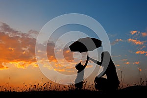 Silhouette of a mother and son holding umbrella and playing outd