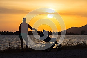 Silhouette of mother with stroller enjoying motherhood at sunset