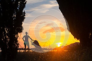 Silhouette of mother with stroller enjoying motherhood at sunset