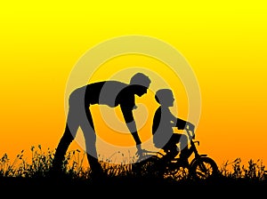 Silhouette of a mother who teaches his son to ride a bike