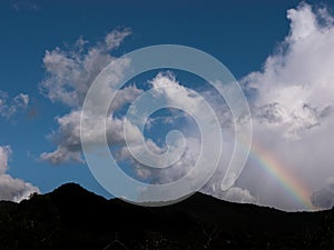 silhouette of mountain with rainbow and clouds