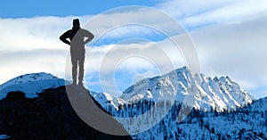 Silhouette of a mountaineer on a rock looks ahead landmark of snowy mountains