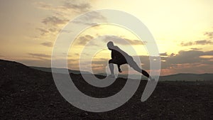 Silhouette of muscular bodybuilder with perfect body posing at the sunrise or sunset in mountains. Handsome strong man