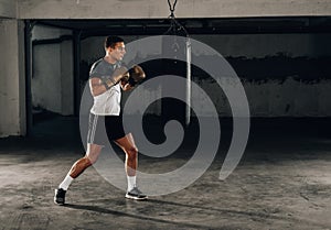 Silhouette muscular fighter training on a punching bag in the gym