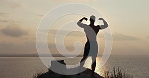 Silhouette of muscular man doing morning exercises on rocky cliff at sunrise