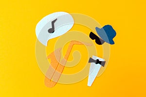 Silhouette of a musician with a saxophone from which melodie flew out, on a yellow background, cutted out of felt. Flat lay. Jazz