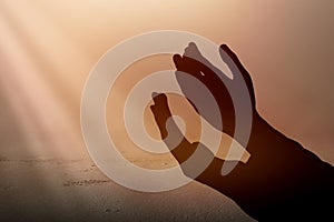 Silhouette of Muslim man standing while raised hands and praying