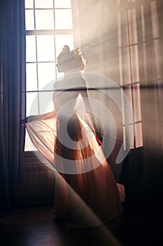 Silhouette of a mysterious fairy woman on the background of the window in the sunlight. Girl in the sunlight of the early morning