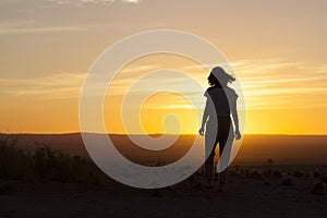 Silhouette o a woman walking into the sunset in the Namibian desert
