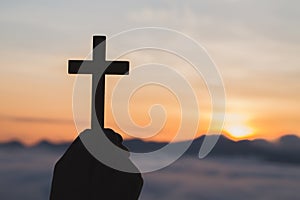 Silhouette off hands holding wooden cross on sunrise background