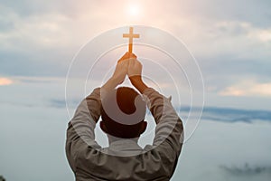Silhouette off hands holding wooden cross on sunrise background