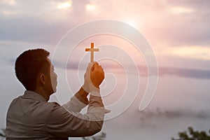 Silhouette off hands holding wooden cross on sunrise background
