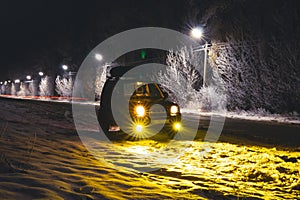 Silhouette off road vehicle is parked on the side of a snowy road. Front view The intercity road is illuminated by LED lanterns.
