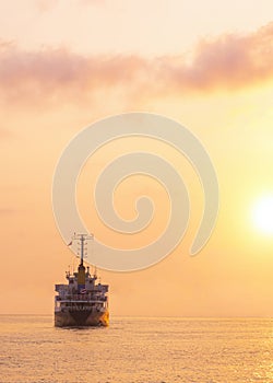 Silhouette Oil Tanker Ship is sailing in the sea with beautiful golden sunlight at sunset time in vertical frame