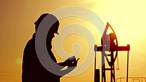 Silhouette of oilfield worker at crude oil pump in the oilfield at golden sunset. Industry, oilfield, people and