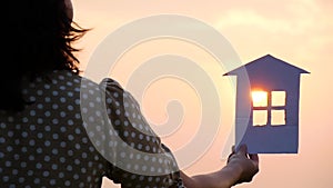 Silhouette of a paper house at sunset. The sun's rays pass through the windows of the paper house. Construction, family