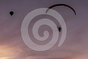 Silhouette of paramotor and hot air balloon against a sky illuminated by the colors of a beautiful sunset