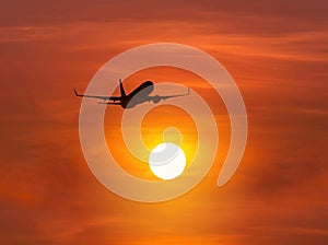Silhouette passenger airplane flying above the sun during sunset