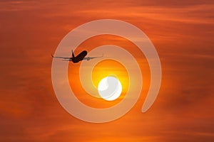 Silhouette passenger airplane flying away in to sky high altitude above the sun during sunset time