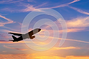 Silhouette passenger airplane flying away in to sky during sunset