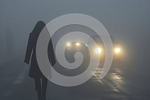 silhouette of pedestrian in fog with cars headlights approaching