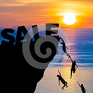 Silhouette of people climbs into cliff to reach the word SALE with sunrise