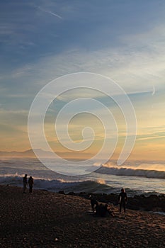 Silhouette of people colorful sunset on atlantic coast with breaking waves with mountain la rhune, capbreton, france