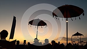 Silhouette People enjoying the sunset view on double six beach in Bali and sitting on sofa cushions and under Balinese umbrellas,