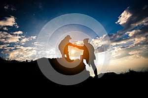 Silhouette of people helping person on the mountain at morning