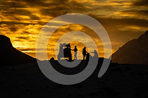 Silhouette of people and a truck having a rest between mountains during a sunset