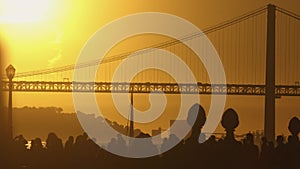 Silhouette of people walking in city - bridge over river and crowd at sunset