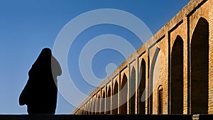 Silhouette of a Persian woman in national dress on the old Khaju Pol-e Khaju bridge in Isfahan. Iran. Ancient Persia.