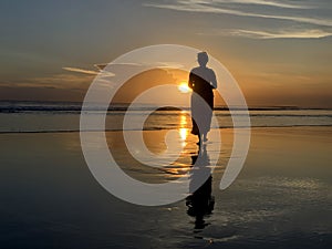 Silhouette of the person in the beach at sunset. A Woman walking alone toward the sun. Fragility concept.