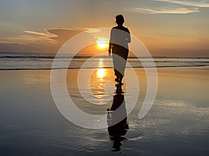 Silhouette of a woman walking alone with bare feet in the beach at sunset.