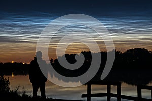 Silhouette of a person looking at noctilucent clouds (NLC), night clouds near a lake in Holland in the evening