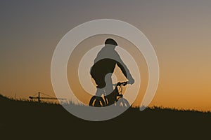 Silhouette of a person riding a bicycle on a field during a sunset