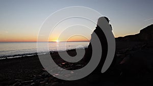 Silhouette of person sitting on a beach watching the sunrise of the sea