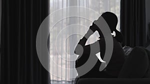 Silhouette of a person suffering from depression in the house, depressed woman sitting alone on the sofa feel stress, sad and