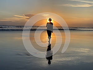 Silhouette of the person walking alone in the beach at sunset. Fragility and loneliness concept.