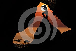 Silhouette photographer in front of the cave near the sea with r