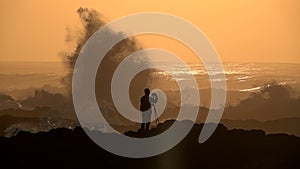Silhouette of Photographer and Slow Motion of Raging Ocean Waves Crashing Rocks during Sunset