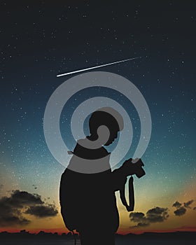 Silhouette of photographer standing in nature background with shooting star and night sky.