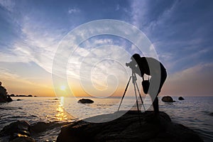 Silhouette a photographer taking pictures of sunrise on a rock,