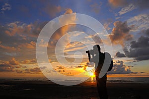 Silhouette a photographer taking pictures of sunrise on a rock,