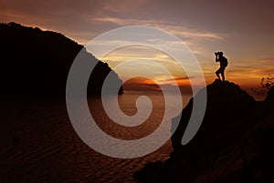 Silhouette of photographer using camera on the top of a rock by the sea , Twilight  sky sunset