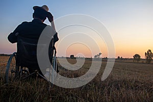 Silhouette Photos young disabled man with field background.He is wearing a hat and sitting on wheelchair photo