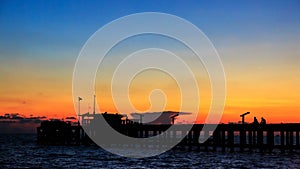 Silhouette of pier, boat with the sun setting in background with cloudy and colorful sky, Starlight sunshine on the water surface