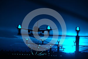 Silhouette of plane landing, runway lights, blue effect