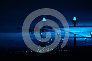 Silhouette of plane landing, runway lights, blue effect